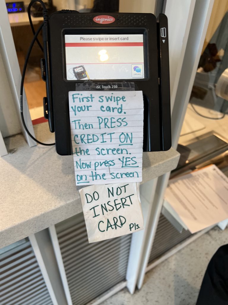 A credit card reader with detailed instructions written on notepads in marker to prevent customer frustration